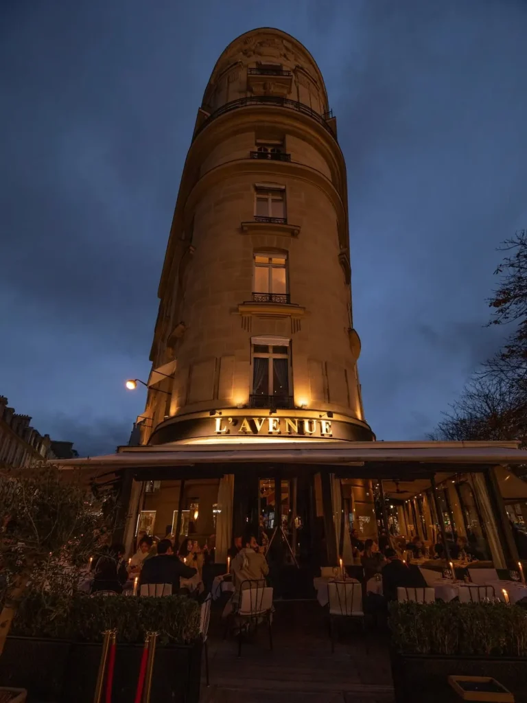 Rounded corner building lit at dusk with the lavenue sign over the candlelit terrace at lavenue Paris