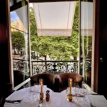 Candlelit table for two set with Avenue menus by an open window over the tree-lined avenue at lavenue Paris
