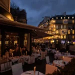 Candlelit terrace tables under the awning with lit Paris buildings beyond at dusk at lavenue Paris