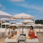 Two guests relaxing on sunbeds under white parasols on the sand at Loulou Restaurant Saint-Tropez