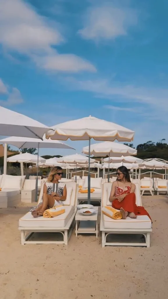 Two guests relaxing on sunbeds under white parasols on the sand at Loulou Restaurant Saint-Tropez
