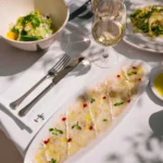 Sea bass carpaccio with herbs and a green salad served with white wine at Loulou Restaurant Saint-Tropez