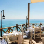 Seafront terrace with white chairs, blue gingham cushions and an open sea view at Loulou Restaurant Saint-Tropez