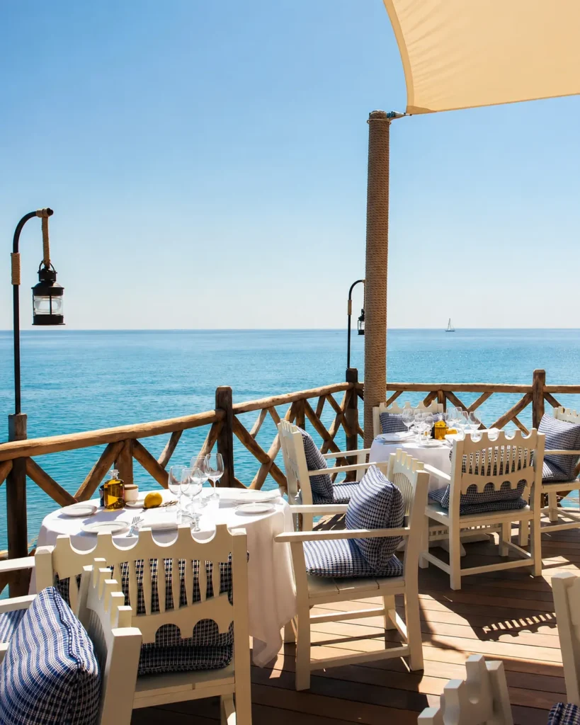 Seafront terrace with white chairs, blue gingham cushions and an open sea view at Loulou Restaurant Saint-Tropez