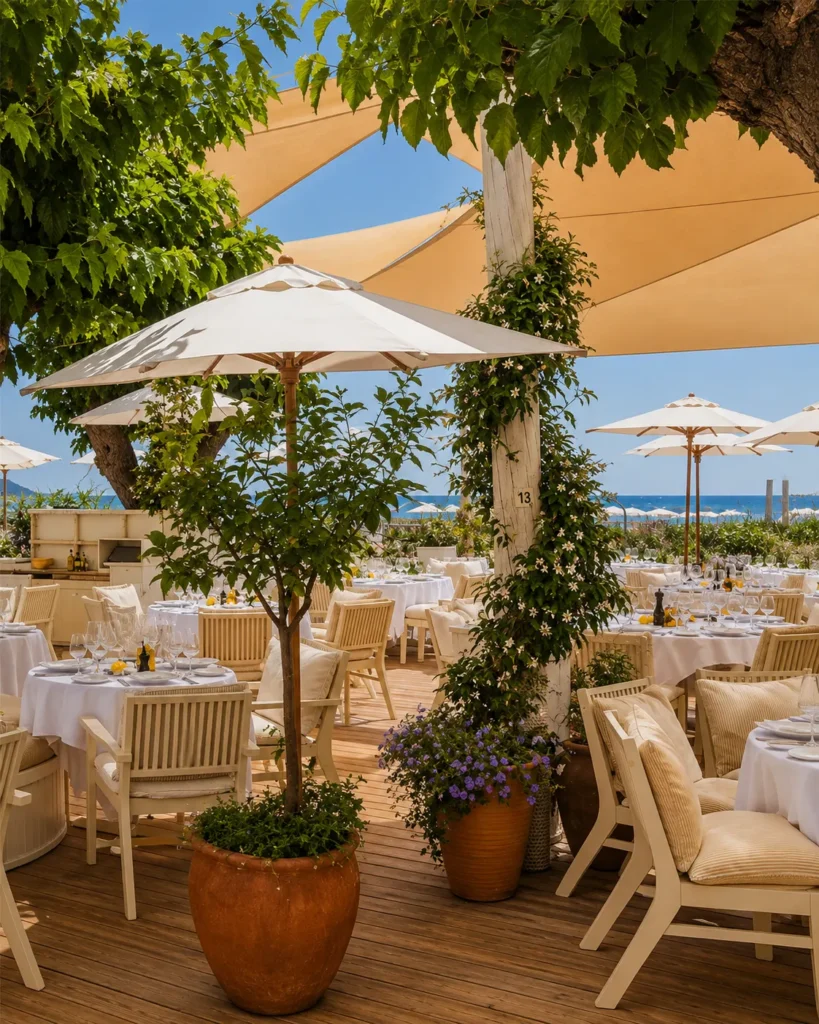 Dining terrace with white parasols, potted trees and sail shades by the sea at Loulou Restaurant Saint-Tropez