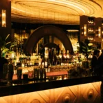 Bar with a mirrored arch and rows of spirits under the golden radial ceiling at Manko Paris