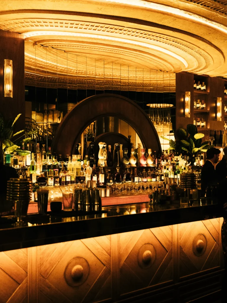 Bar with a mirrored arch and rows of spirits under the golden radial ceiling at Manko Paris