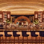 Back bar of bottles beneath a golden radial dome ceiling with blue patterned stools at Manko Paris