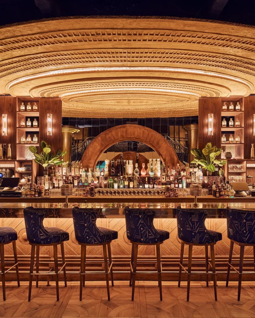Back bar of bottles beneath a golden radial dome ceiling with blue patterned stools at Manko Paris