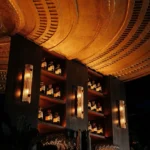 Ribbed glass sconces and bottle shelves beneath the curved gold ceiling at Manko Paris