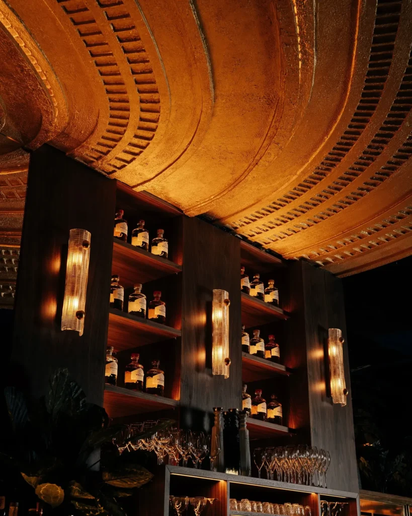 Ribbed glass sconces and bottle shelves beneath the curved gold ceiling at Manko Paris