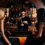 Bartender straining a cocktail for two guests at the arched bar at Manko Paris