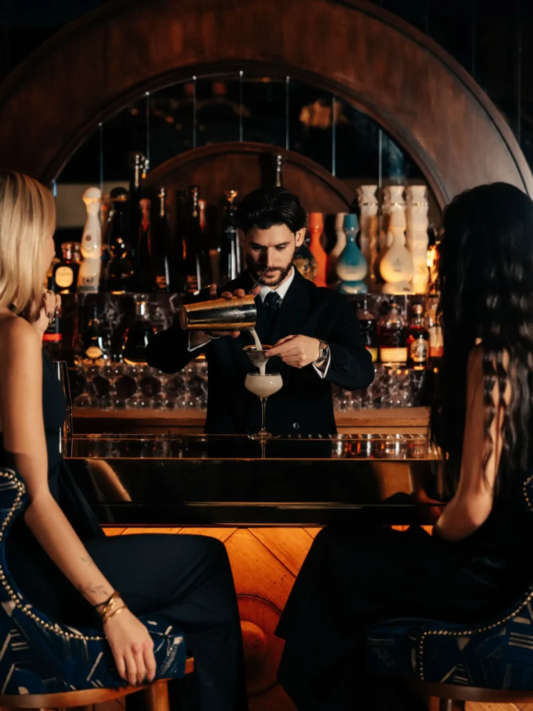 Bartender straining a cocktail for two guests at the arched bar at Manko Paris