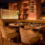 Ochre banquette and carved-back chairs by a gilded lattice screen at Manko Paris
