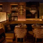 Set tables around a curved ochre banquette with a brass sconce and bottle shelves at Manko Paris