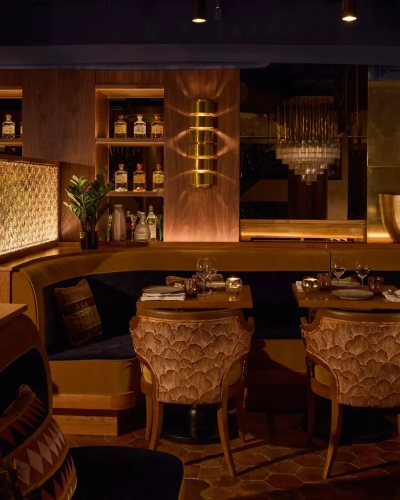 Set tables around a curved ochre banquette with a brass sconce and bottle shelves at Manko Paris