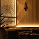 Corner banquette lit by a glowing patterned lattice window with a gold shell sconce at Manko Paris