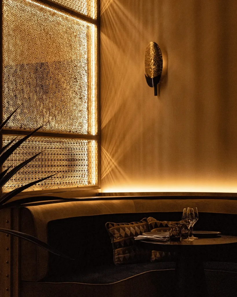 Corner banquette lit by a glowing patterned lattice window with a gold shell sconce at Manko Paris