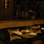 Candlelit banquette table with printed cushions beneath a brass sconce and planters at Manko Paris