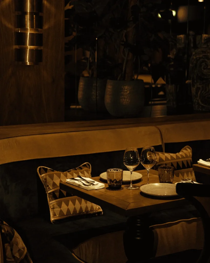 Candlelit banquette table with printed cushions beneath a brass sconce and planters at Manko Paris