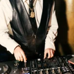 DJ in a leather vest and gold chain mixing at the decks at Manko Paris