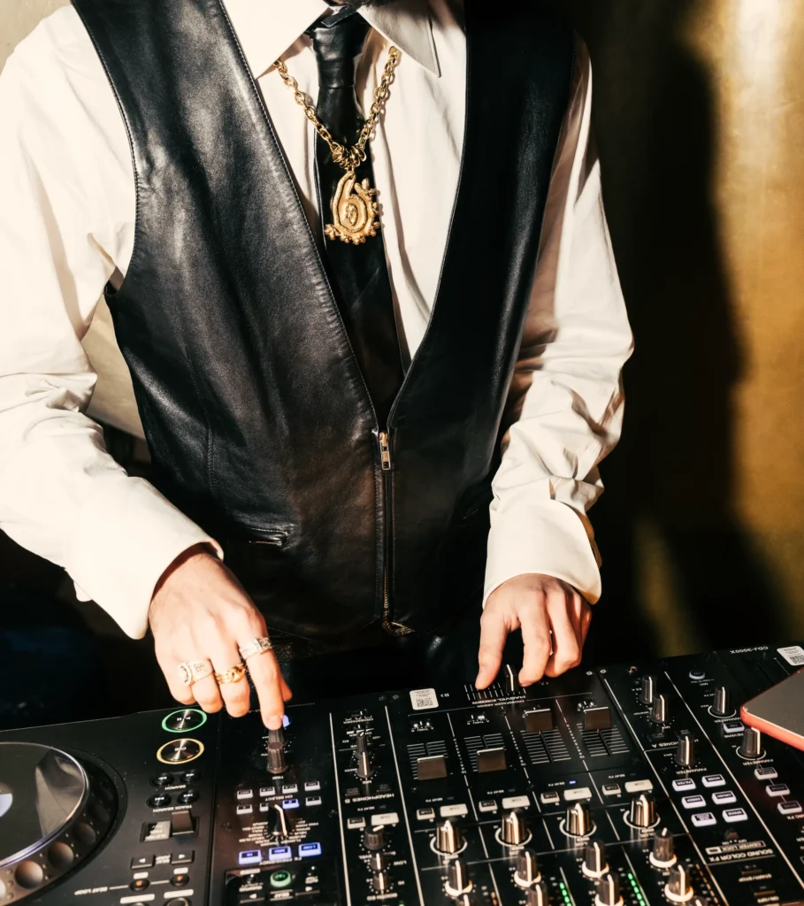 DJ in a leather vest and gold chain mixing at the decks at Manko Paris
