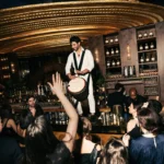 Performer in white playing a djembe atop the bar before a crowd under the gold ceiling at Manko Paris