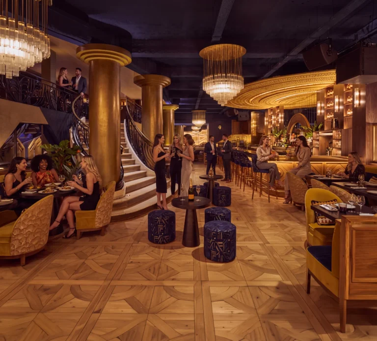 Grand Art Deco room with a sweeping gold staircase, tiered chandeliers and guests at Manko Paris