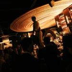Silhouetted drummer on the bar backlit by the golden radial ceiling amid a crowd at Manko Paris