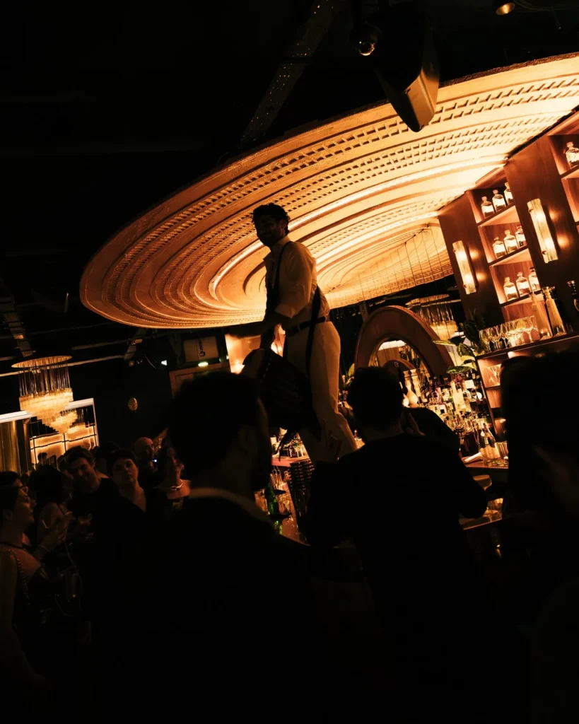 Silhouetted drummer on the bar backlit by the golden radial ceiling amid a crowd at Manko Paris