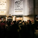 Gold MANKO lettering on the marble facade above a crowd at the 15 Montaigne entrance at night at Manko Paris