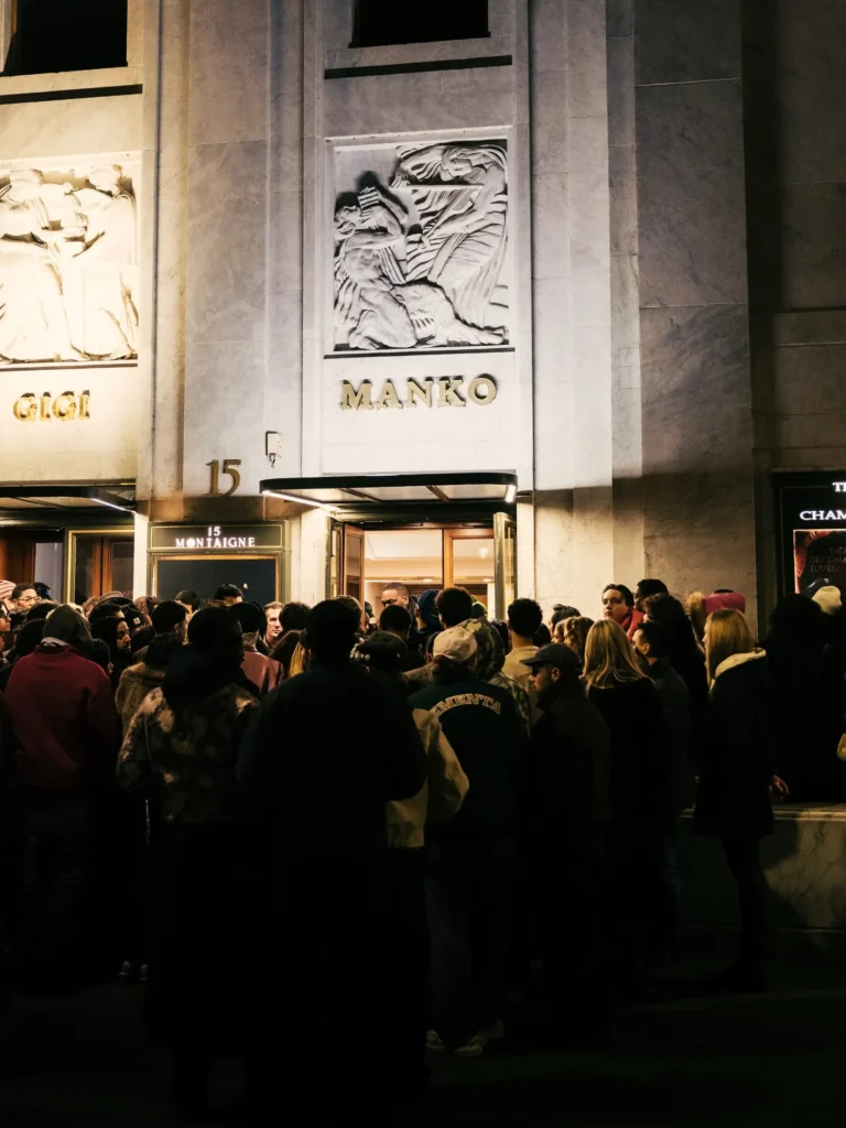Gold MANKO lettering on the marble facade above a crowd at the 15 Montaigne entrance at night at Manko Paris