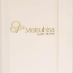 Gold Matsuhisa Saint-Tropez logo on a cream wall