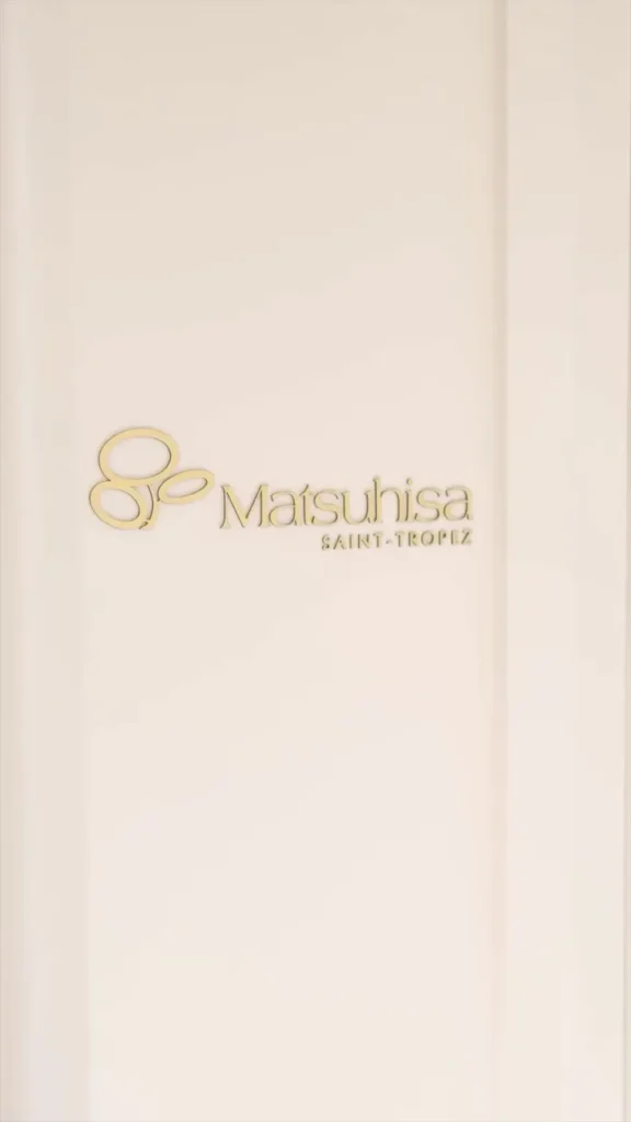 Gold Matsuhisa Saint-Tropez logo on a cream wall