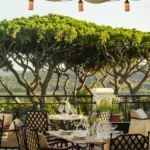 Set terrace tables framed by umbrella pines and a wrought-iron balustrade at Matsuhisa Saint-Tropez
