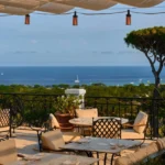 Terrace tables under a canopy with an umbrella pine and sea view at Matsuhisa Saint-Tropez