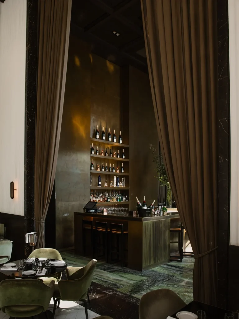 Tall curtained bar with backlit bottle shelves and green marble floor at Monsieur Bleu Paris