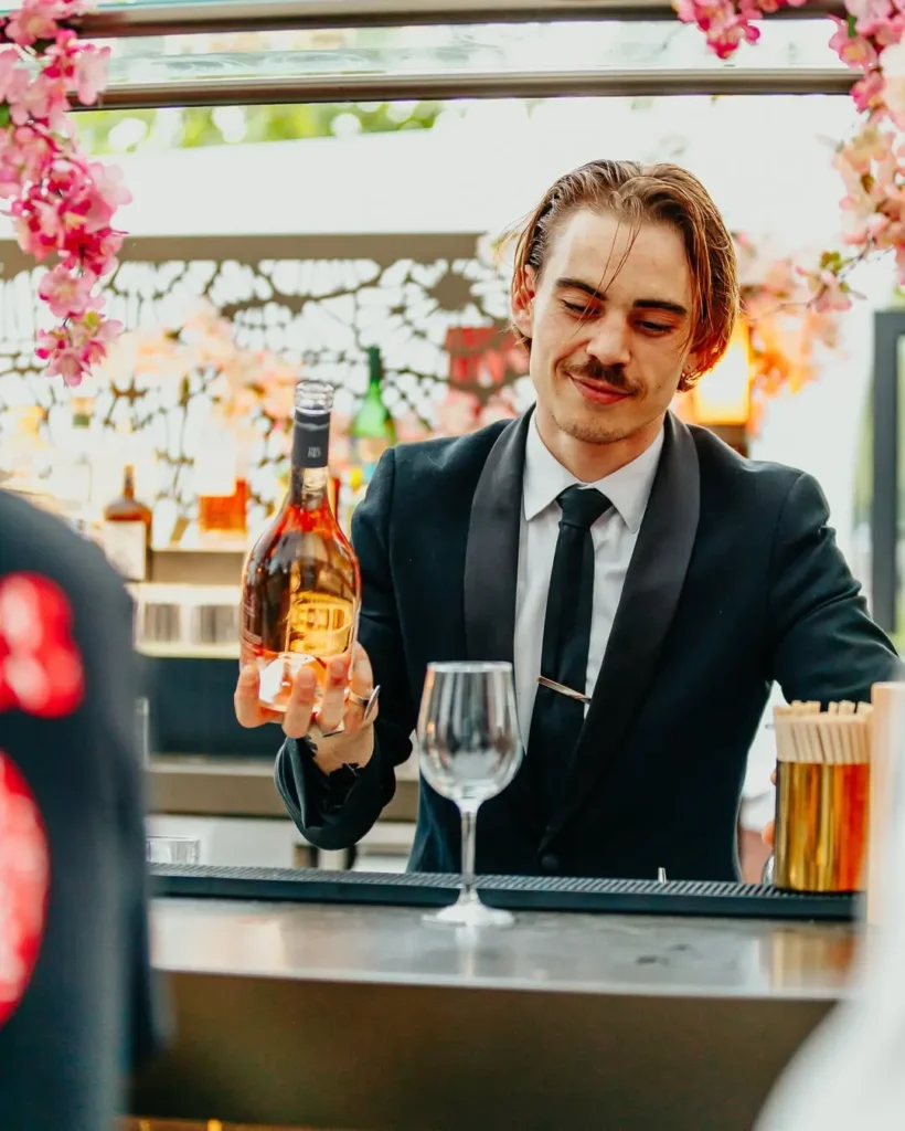 Bartender presenting a bottle of rosé at a blossom-framed bar at Monsieur Bleu Paris