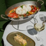 Burrata over heirloom tomatoes in a silver dish beside a crab terrine at Monsieur Bleu Paris
