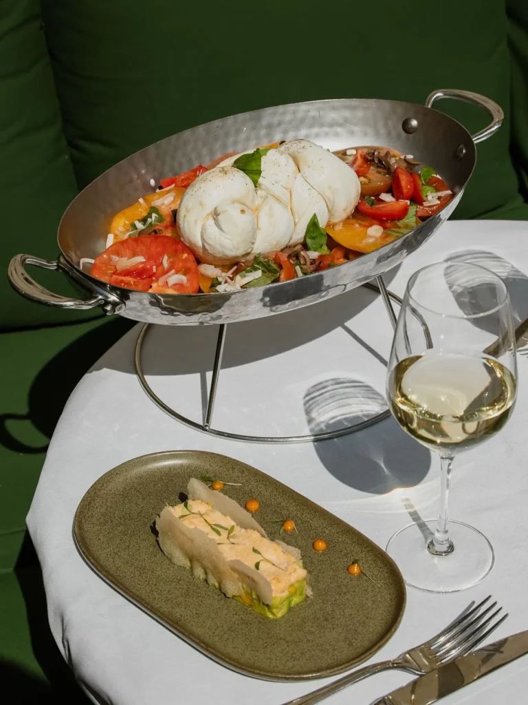 Burrata over heirloom tomatoes in a silver dish beside a crab terrine at Monsieur Bleu Paris