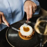Caramel-filled tart with a cream dome being cut, served with white wine at Monsieur Bleu Paris