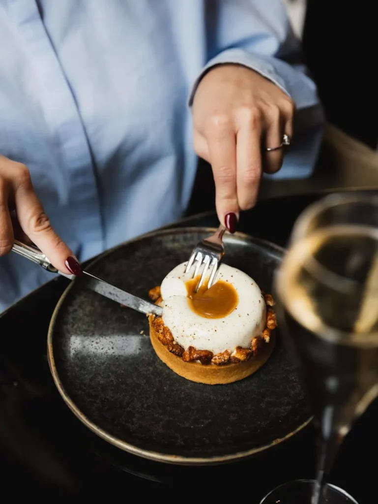 Caramel-filled tart with a cream dome being cut, served with white wine at Monsieur Bleu Paris