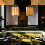Yellow velvet banquettes and fluted white pillars under large lantern pendants at Monsieur Bleu Paris