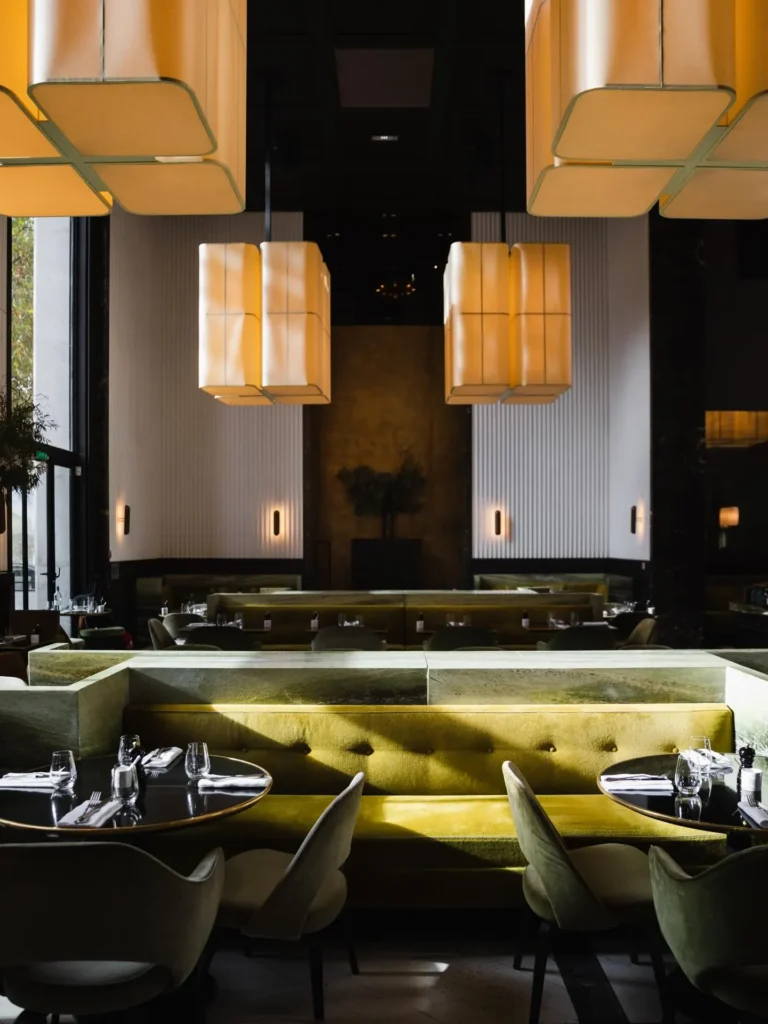 Yellow velvet banquettes and fluted white pillars under large lantern pendants at Monsieur Bleu Paris