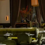 Dining room with green banquettes, curtained bar and an autumn tree centrepiece at Monsieur Bleu Paris