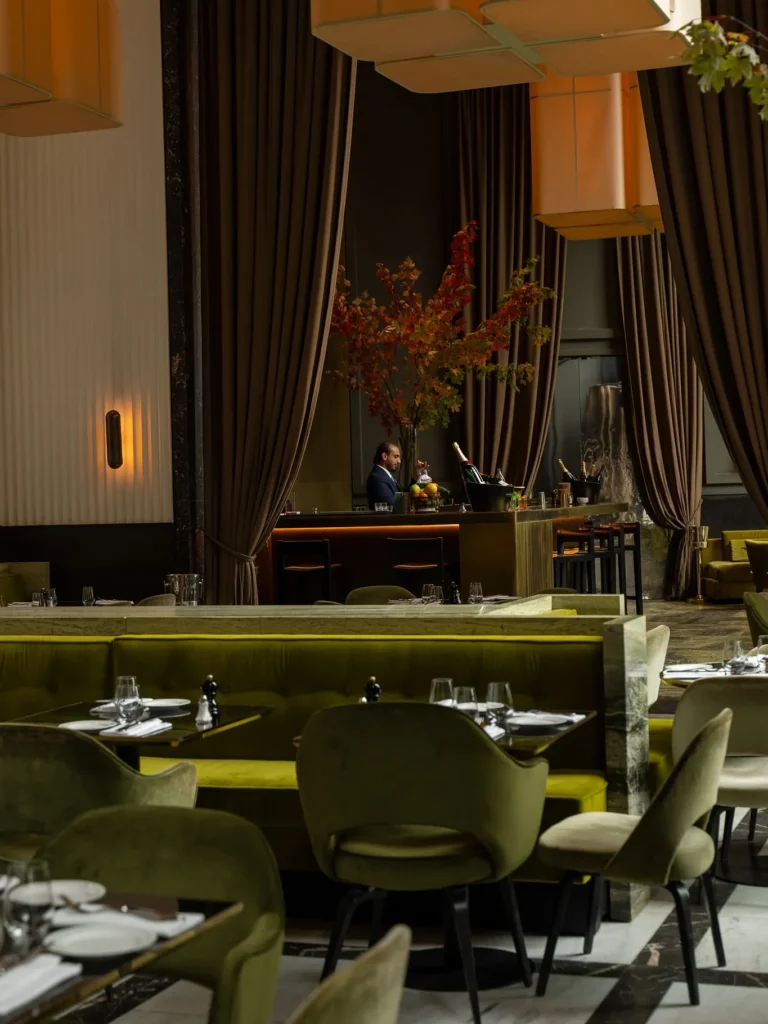 Dining room with green banquettes, curtained bar and an autumn tree centrepiece at Monsieur Bleu Paris
