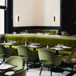 Green velvet banquette and armchairs by a fluted wall with brass sconces at Monsieur Bleu Paris