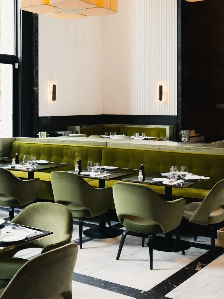 Green velvet banquette and armchairs by a fluted wall with brass sconces at Monsieur Bleu Paris