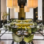Art Deco dining room with green and yellow velvet seating, tall fabric pendants and a checkerboard floor at Monsieur Bleu Paris