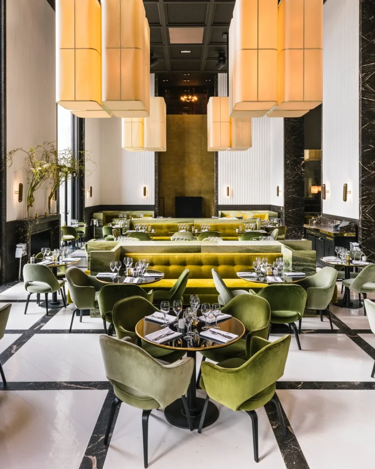 Art Deco dining room with green and yellow velvet seating, tall fabric pendants and a checkerboard floor at Monsieur Bleu Paris